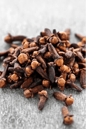 Tas de clous de girofle séchés sur une table en bois, connus pour leur arôme puissant et leurs bienfaits antimicrobiens.