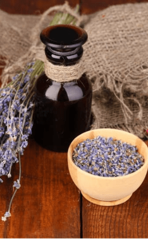 Flacon en verre foncé contenant de l'huile essentielle de lavande, accompagné de fleurs de lavande séchées dans un bol en bois