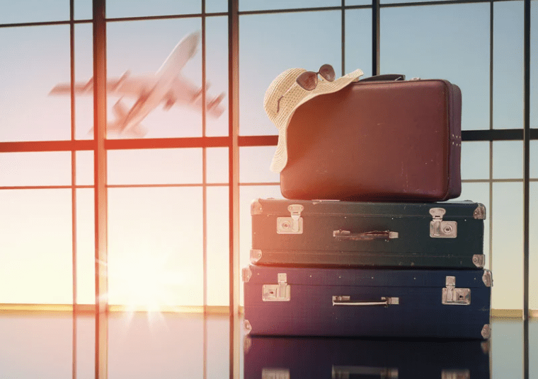 Bagages empilés avec un chapeau et des lunettes de soleil à l'aéroport, avec un avion au décollage en arrière-plan.