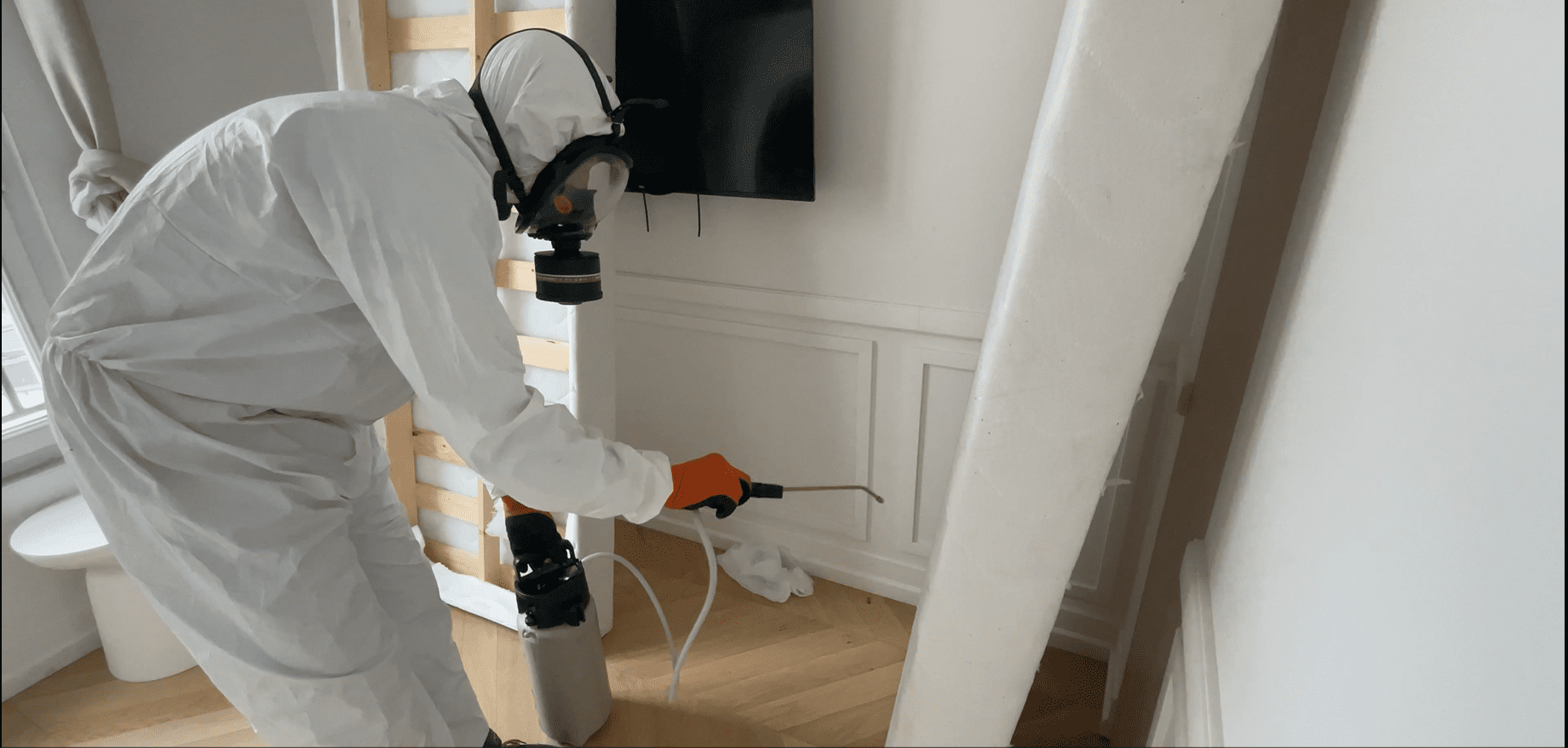 Un technicien en combinaison de protection pulvérisant un traitement dans une pièce contre les punaises de lit.