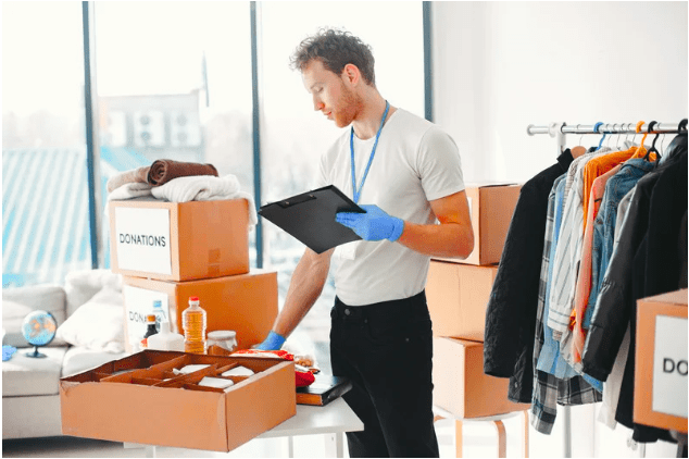 Homme réalisant un inventaire précis de vêtements et cartons dans une pièce remplie de dons
