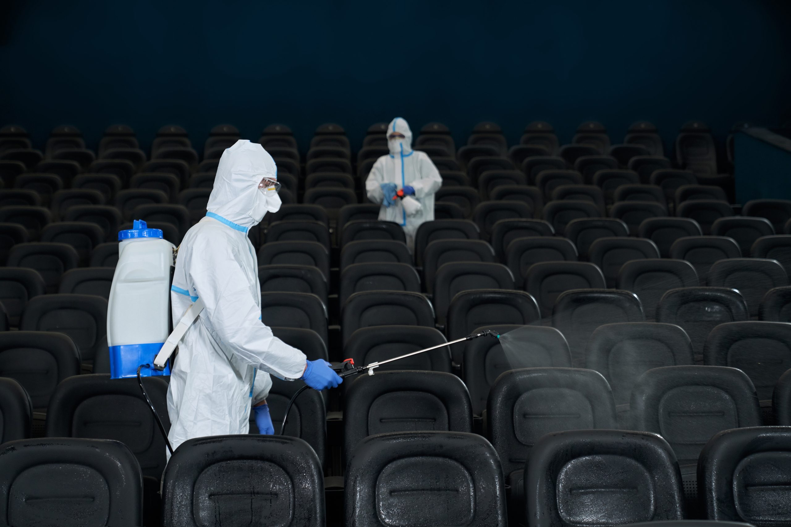 Travailleurs en combinaison de protection désinfectant une salle de cinéma, pulvérisant des produits spéciaux sur les sièges pour éliminer les punaises de lit et autres nuisibles.