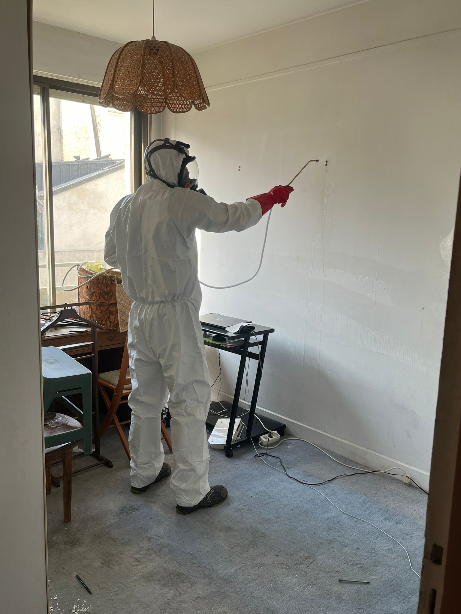 Technicien en combinaison pulvérisant un produit sur un mur pour traiter une infestation de punaises de lit.
