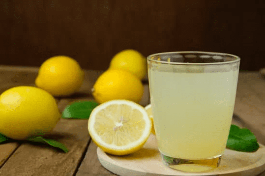 Verre de jus de citron frais avec des citrons en arrière-plan, un remède naturel contre les punaises de lit.